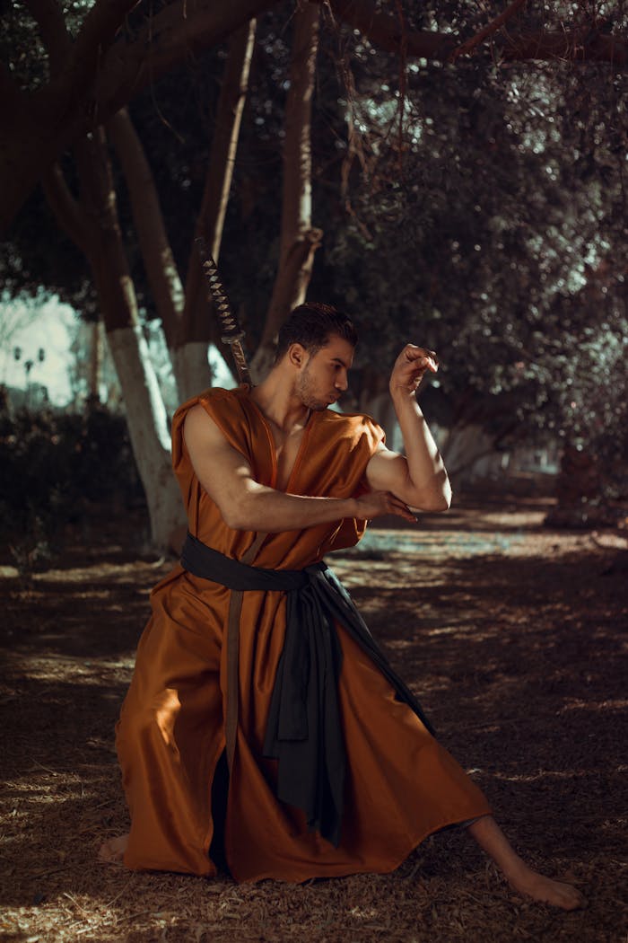 Martial artist in traditional brown robe posing under trees, showcasing strength and concentration.